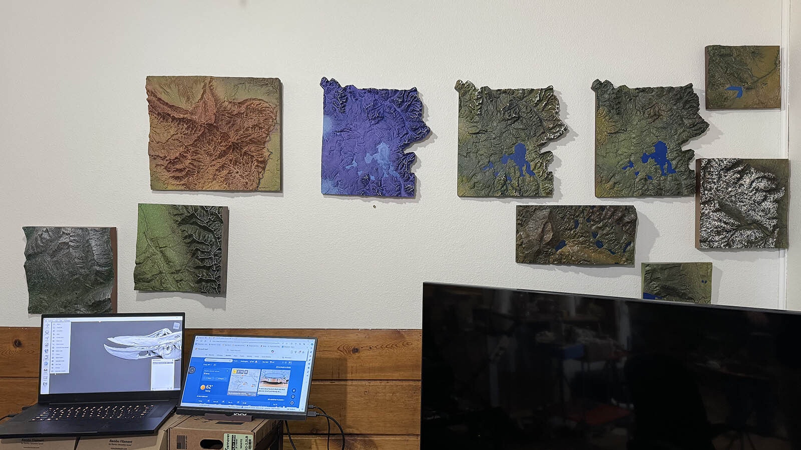 A wall of 3D-printed topographic maps at the Maps and Skulls studio in Cody. The three maps in the middle were printed and painted to resemble Yellowstone National Park.