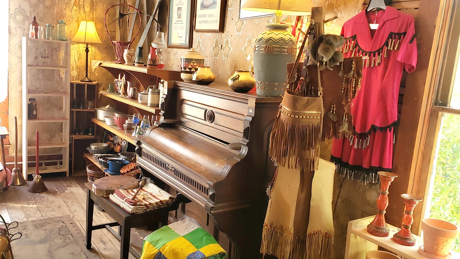 An antique piano sits between old china and a jingle dress and leather purse upstairs in the Aladdin General Store.