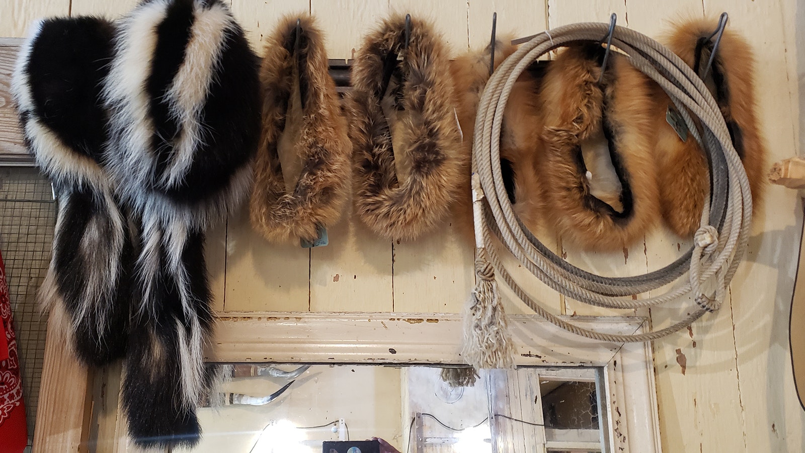 Fur hats hang in a row with a used rope next to colorful new bandanas.