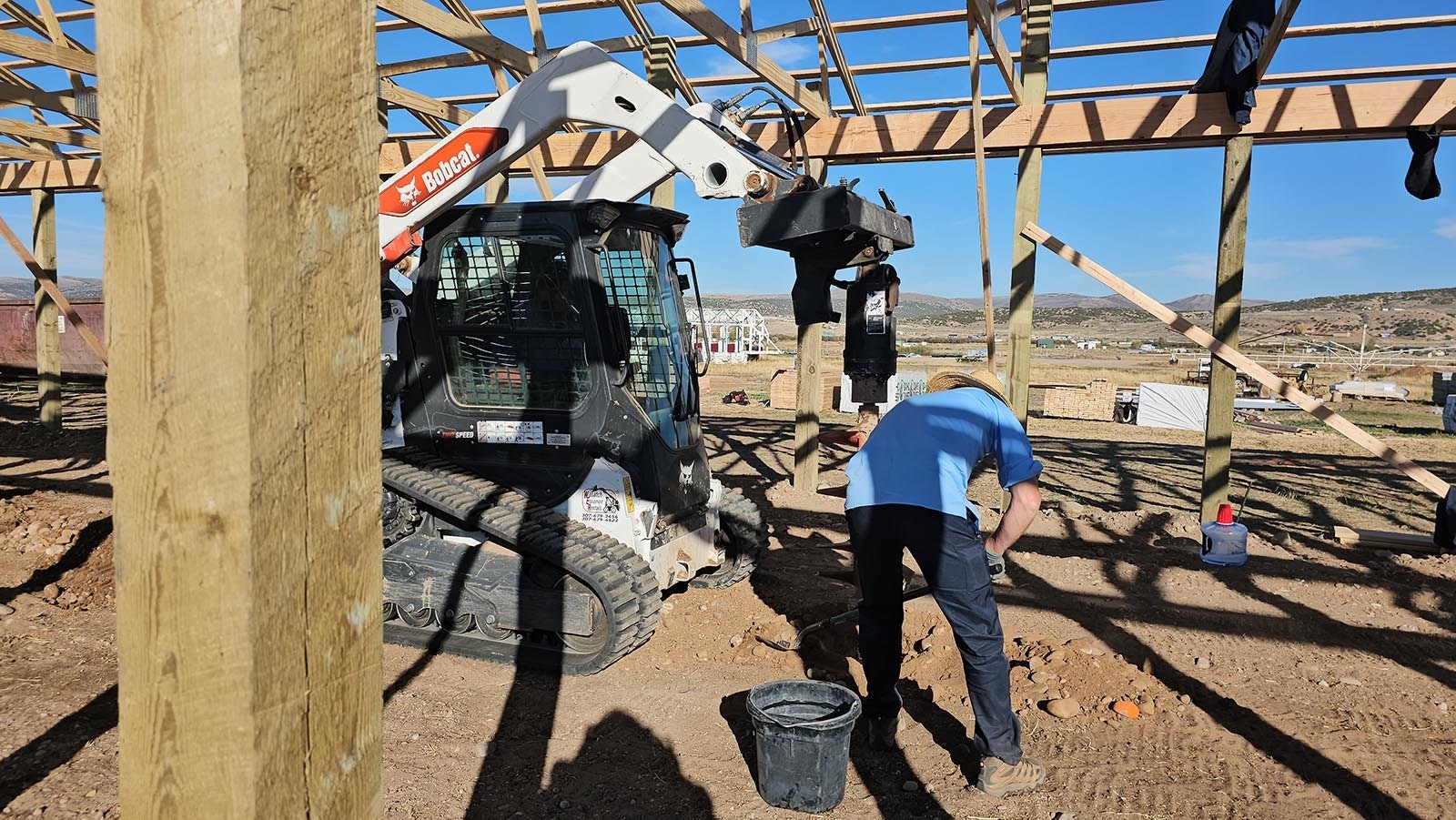 One Amish man shovels some dirt and rocks out of the way, as another prepares to drill a 4-foot hole for a support beam.