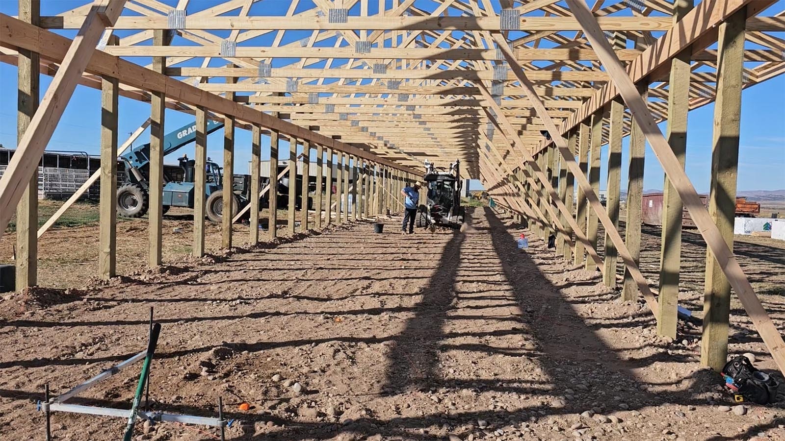 One Amish man shovels some dirt and rocks out of the way, as another prepares to drill a 4-foot hole for a support beam.