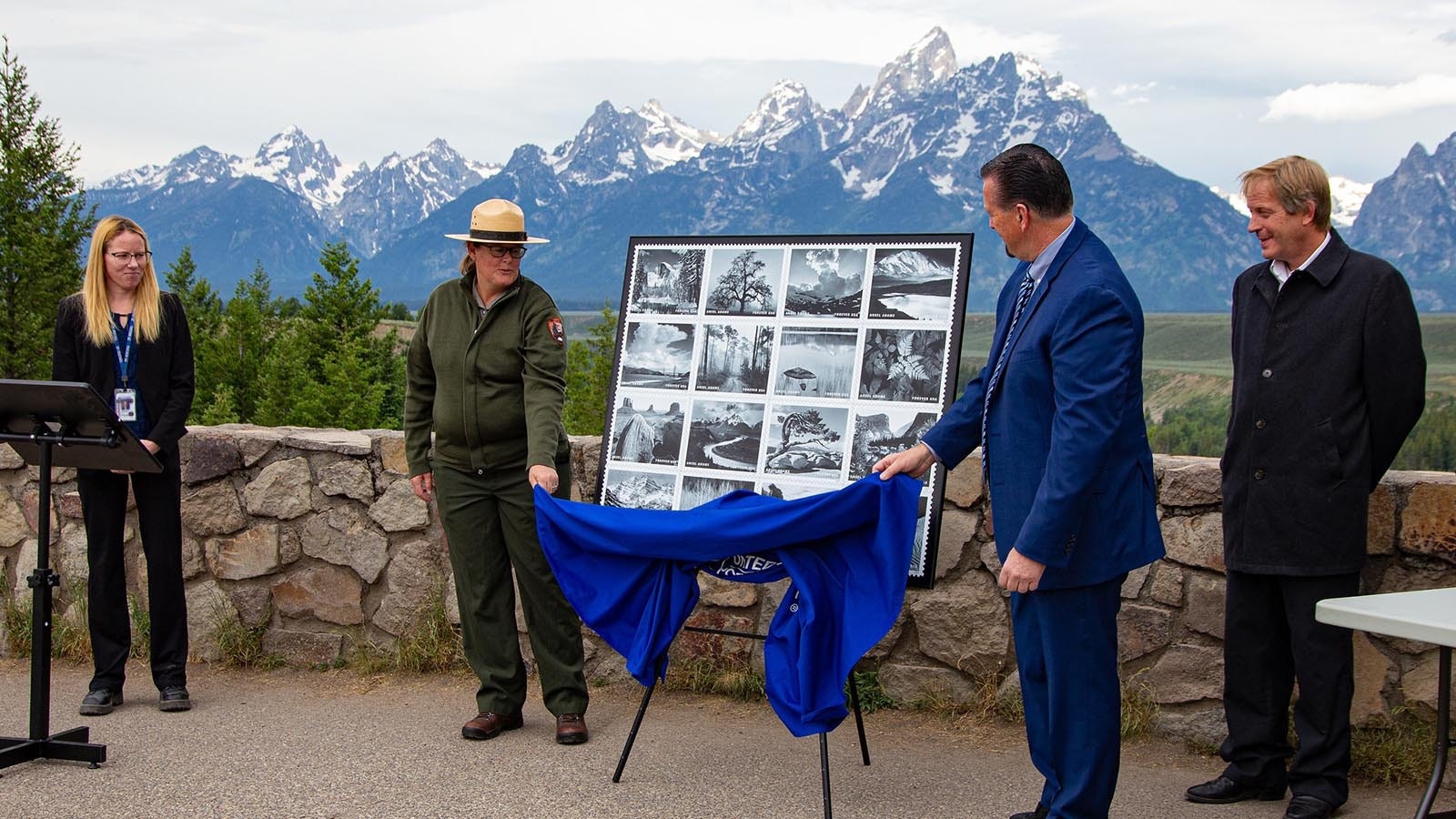 Moose, Wyoming, Postmaster Aleicia Dickson, from left, Acting Grand Teton National Park Deputy Superintendent Robin Martin, postal operations manager for Wyoming Sean Moore, Park Ranger Helen Bennett and USPS District Manager Douglas Smith unveil the new flight of Ansel Adams stamps in front of the Grand Tetons in Wyoming.