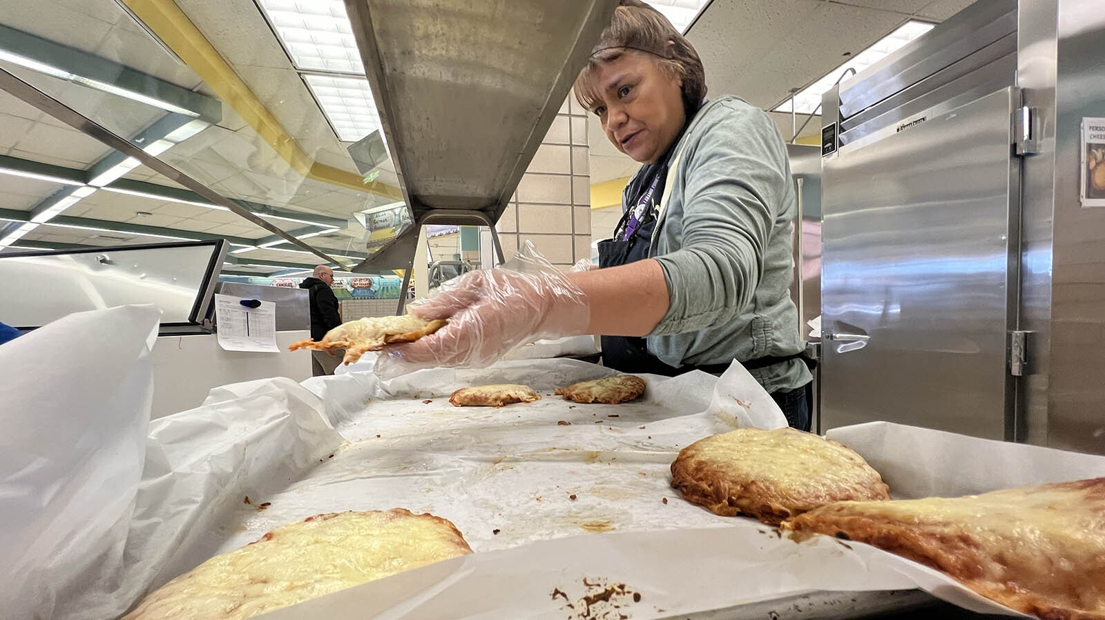 Frances Vigil reaches through the severing line to dish out homemade pizza at Arp Elementary School in Cheyenne.