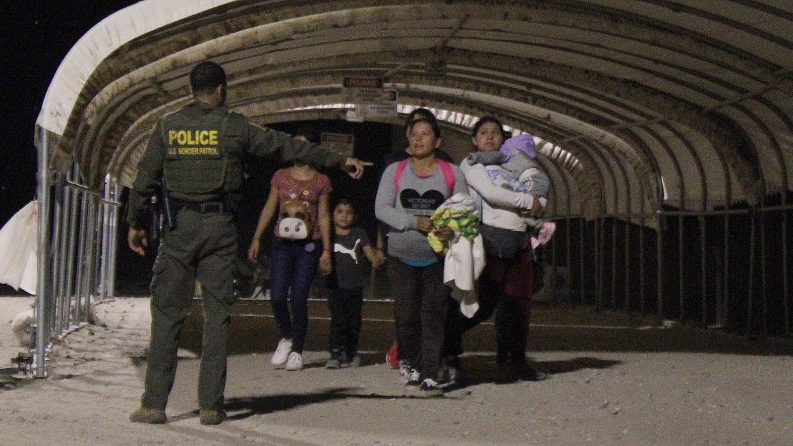 The Border Patrol agent instructs the immigrants to stand facing the wall.