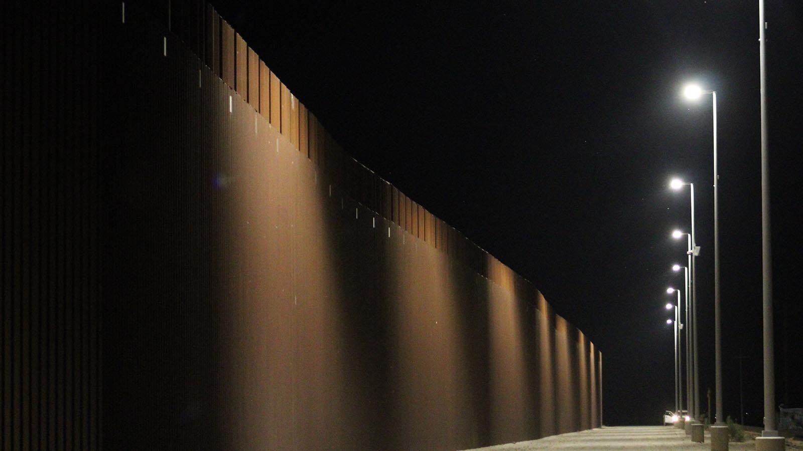 The southern border wall is about 30-feet tall and made up by closely separated, dark red bars.