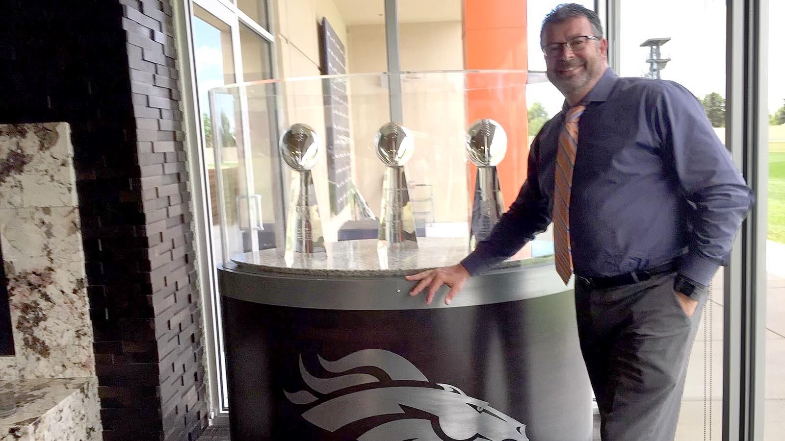 Former Denver radio host, and Wyoming native, John Baggett stands in front of the Denver Broncos' three Vince Lombardi trophies.