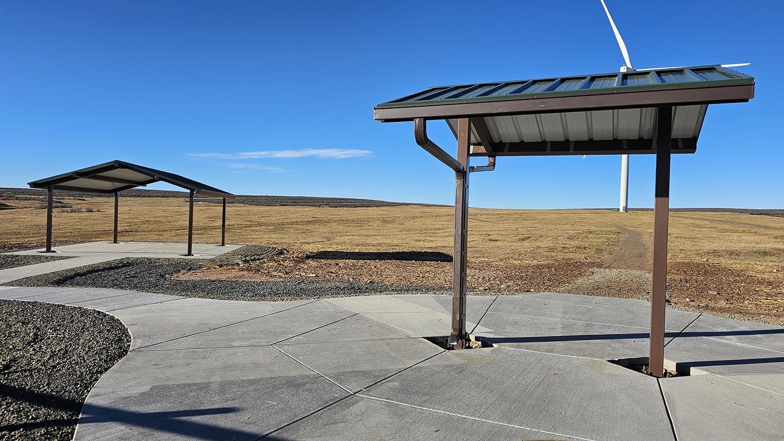 The structure on the left at the Belvoir Ranch will have picnic tables while the structure on the right will have maps. A wind turbine is visible in the background, but the turbines all disappear as users take to the trails, thanks to their orientation.