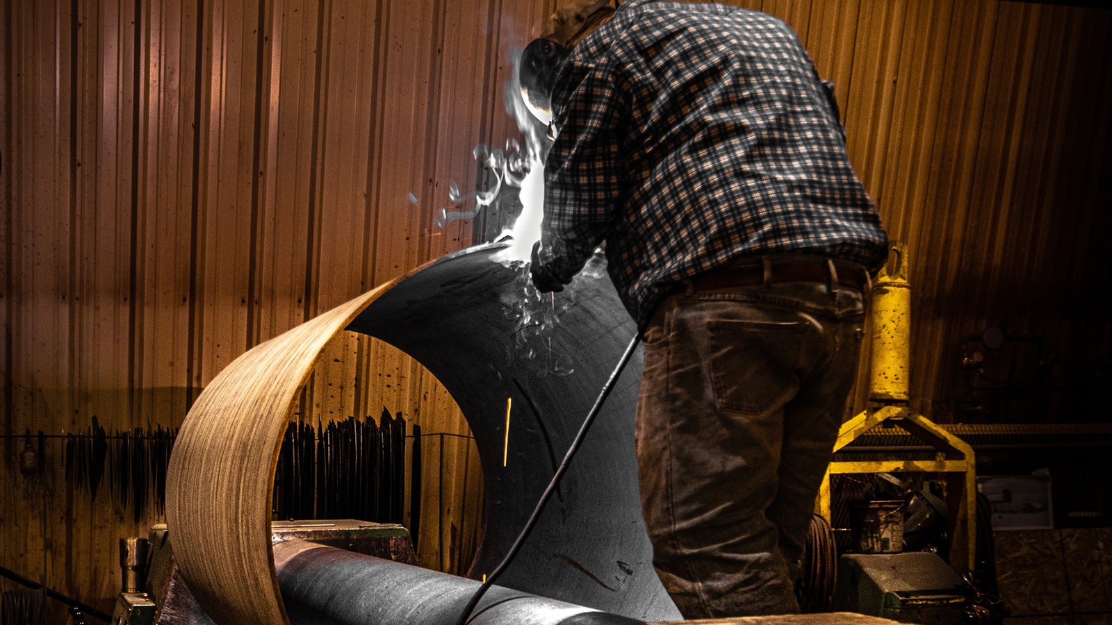 A worker at High Country Fabrication works on turning a flat sheet of steel into a rounded vessel in the roller area.