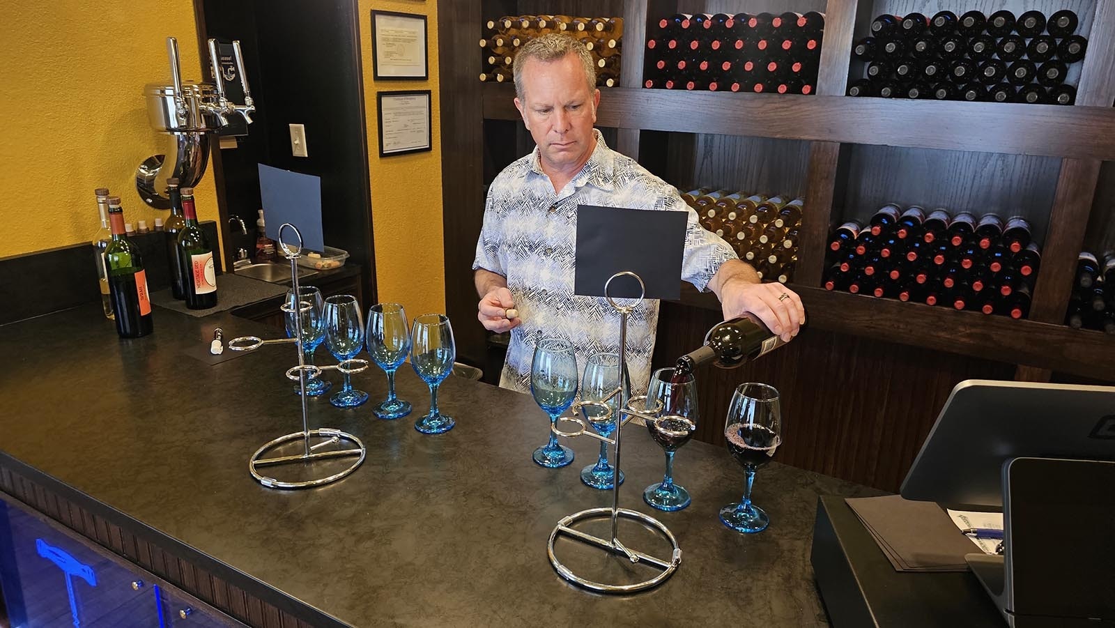 Brandon Erdmann pours glasses of wine for a tasting flight at Blue Stem Wine House. the glasses will go into the spiral holder, along with a notecard that labels each wine in order.