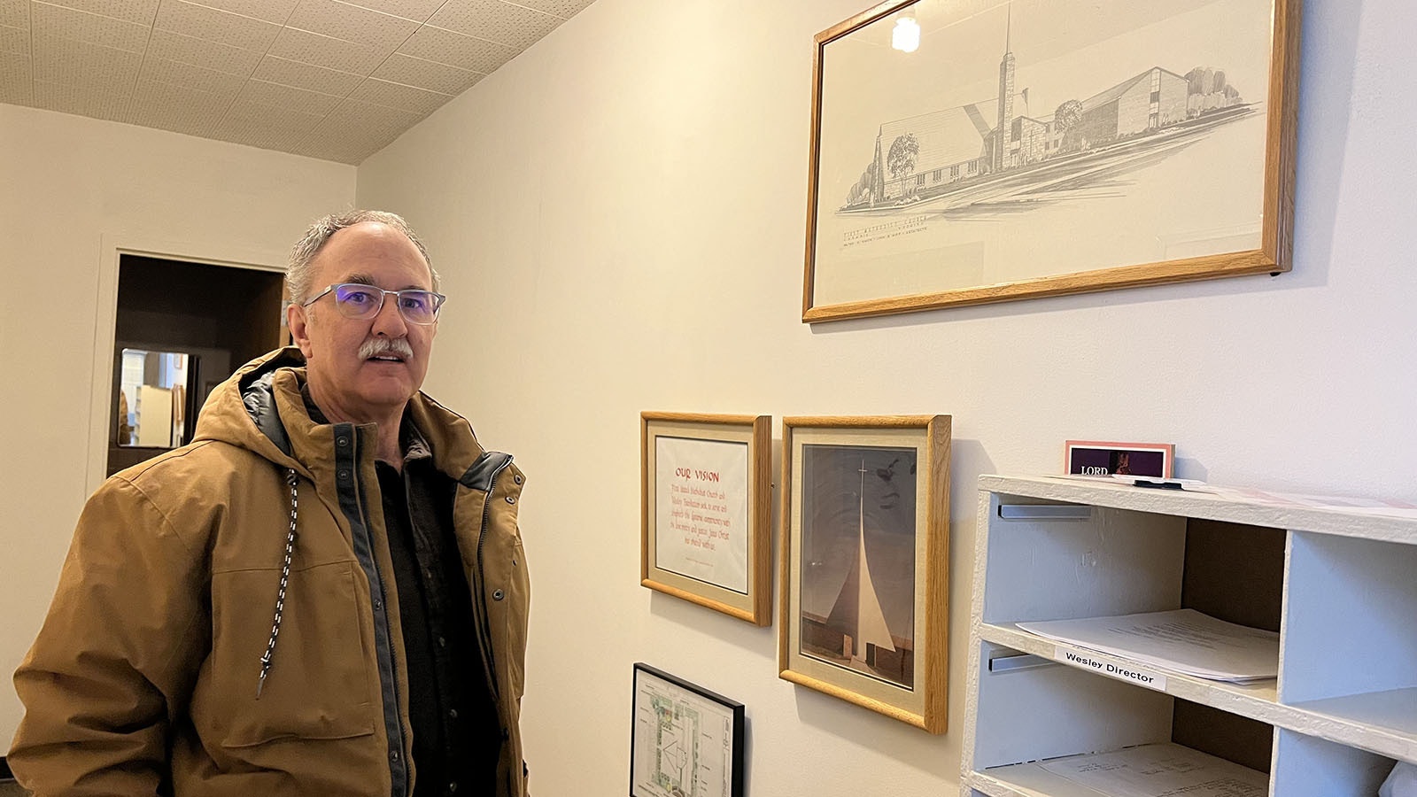 Pastor Eric Feuerstein of the First United Methodist Church in Laramie stands next to a drawing of the original, much more subtle design for the church’s iconic sanctuary.