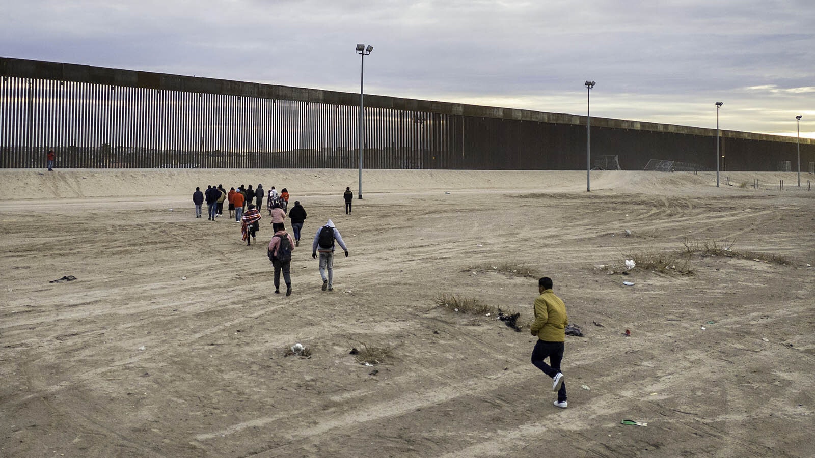 Immigrants run towards the U.S.-Mexico border wall after crossing the Rio Grande into El Paso, Texas on Feb. 1, 2024, from Ciudad Juarez, Mexico. They had also passed through razor wire set by Texas National Guard troops to proceed for processing by U.S. Border Patrol agents.