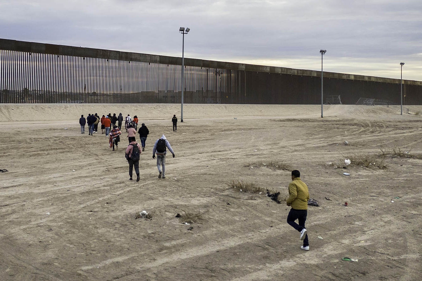 Immigrants run towards the U.S.-Mexico border wall after crossing the Rio Grande into El Paso, Texas on Feb. 1, 2024, from Ciudad Juarez, Mexico. They had also passed through razor wire set by Texas National Guard troops to proceed for processing by U.S. Border Patrol agents.