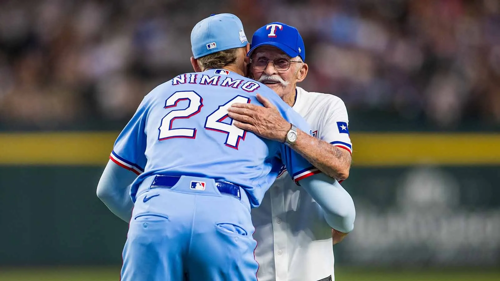 Brandon Nimmo, No. 24 of the Texas Rangers, hugs his grandfather Darrel Nimmo after Darrel threw out the ceremonial first pitch before a game against the Cleveland Guardians at Globe Life Field on June 7, 2026, in Arlington, Texas.