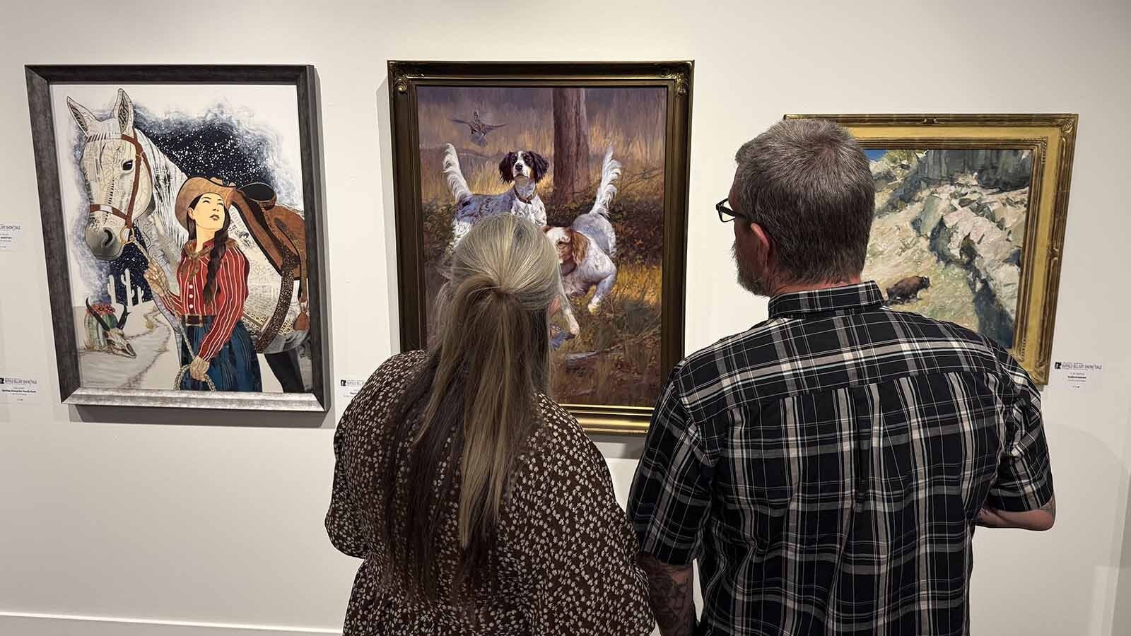 Visitors admire three paintings on display at the Buffalo Bill Center of the West as part of the 44th Buffalo Bill Art Show and Sale.