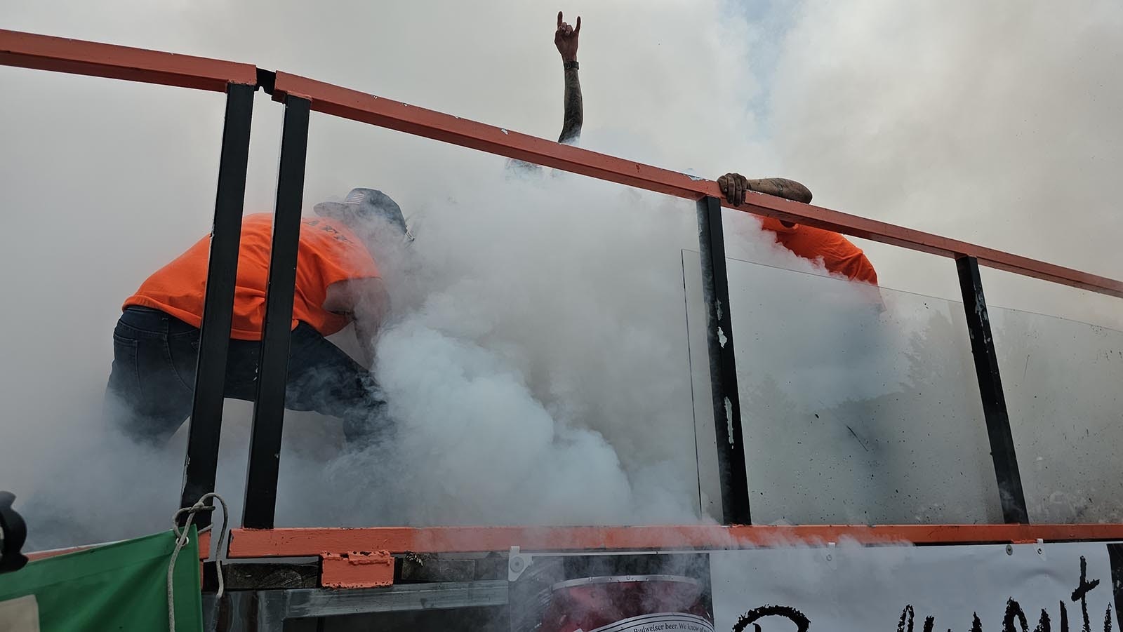 Smoke from the Burnout envelops the rider and crew. One member of the Burnout team braces the bike so it doesn't go anywhere, while a second sprays the tire with water to prevent friction from starting a fire.