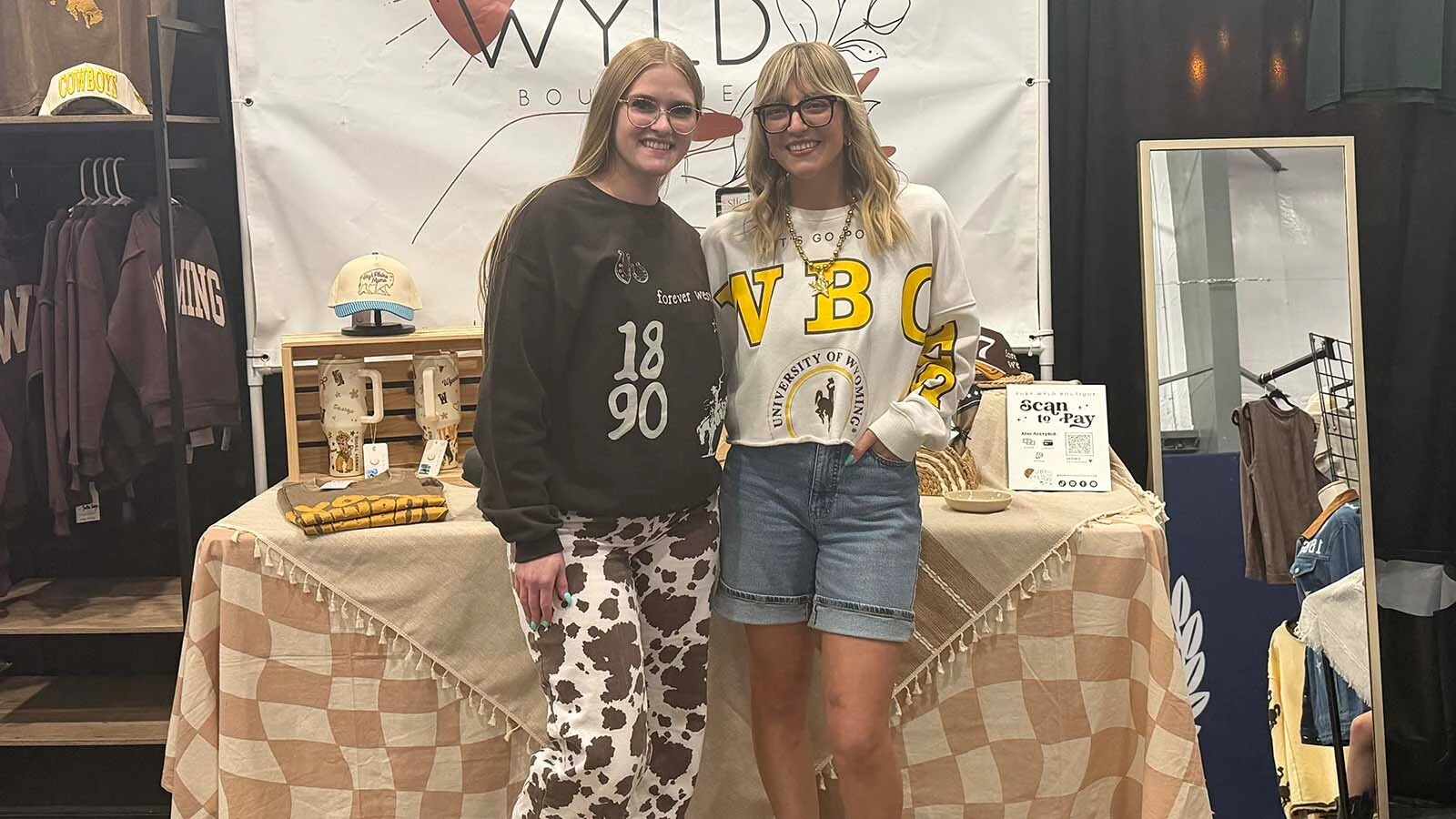 Ruby Wyld Boutique staff pose inside their booth at the CNFR vendor expo. The boutique specializes in western-inspired apparel that mixes rodeo culture with contemporary fashion trends.