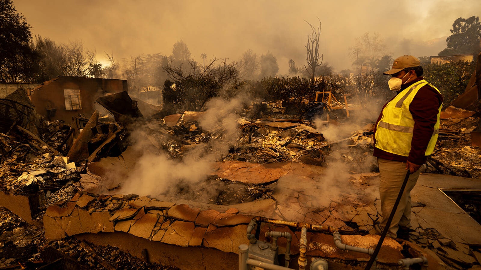 A man sprays water on the remains of a home that burned in the Eaton Fire in Altadena, California. Powerful Santa Ana winds are pushing wildfires across the region, killing at least 24 people so far.