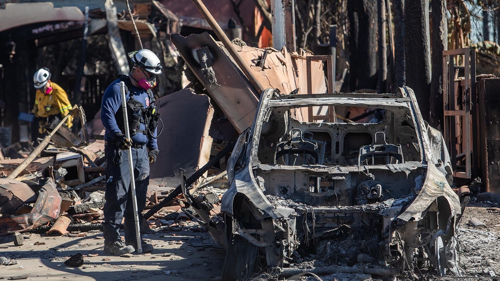 A Firefighter looks at a burned car while his college inspects a burned house from the Palisades Fire in the Pacific Palisades neighborhood on Jan. 15, 2025, in Los Angeles, Calif. Multiple wildfires fueled by intense Santa Ana winds continue to burn across Los Angeles County, with some containment achieved. At least 25 people have died, more than 12,000 structures have been destroyed or damaged and 40,000 acres burned. More than 88,000 people remain under evacuation orders.