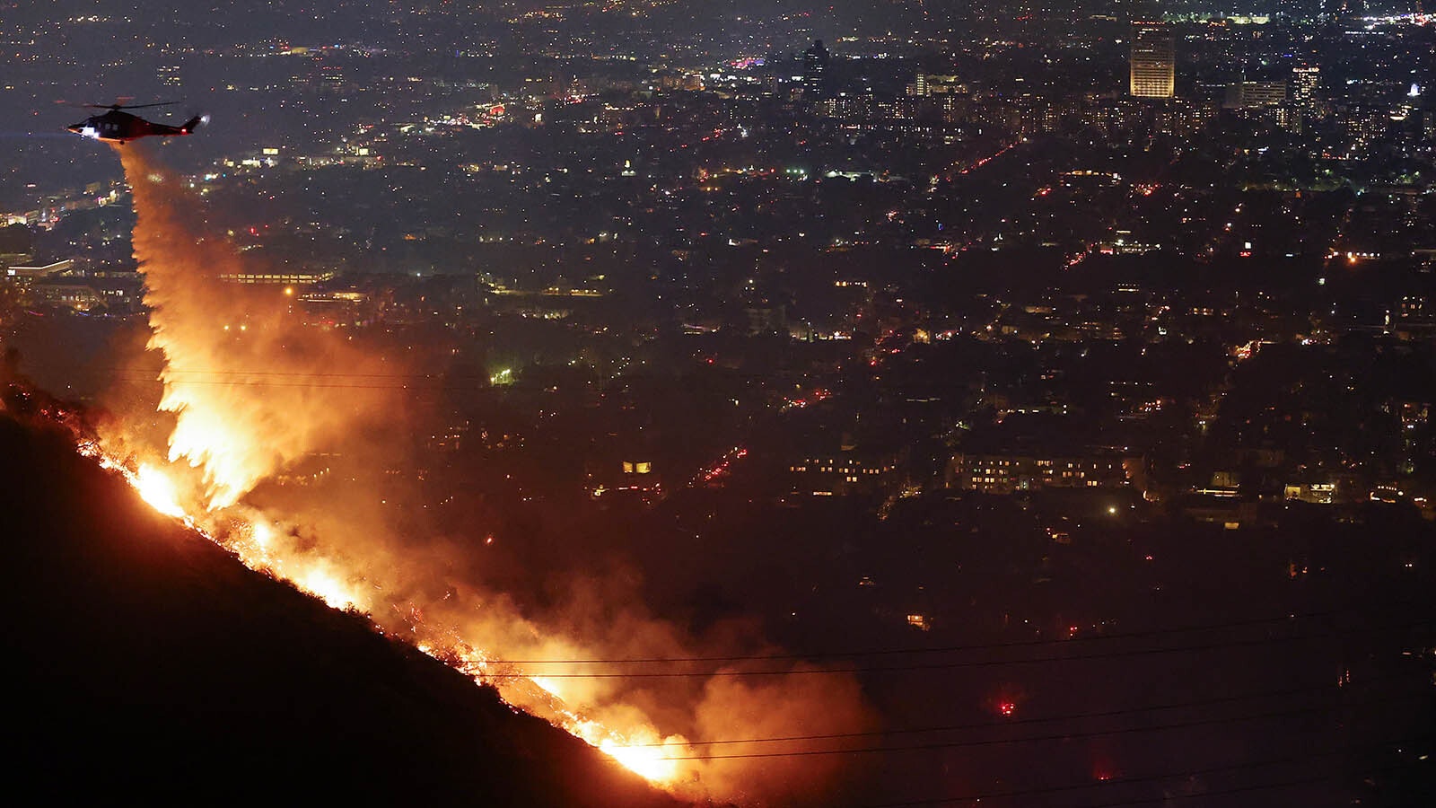 A firefighting helicopter drops water as the Sunset Fire burns in the Hollywood Hills of Southern California.