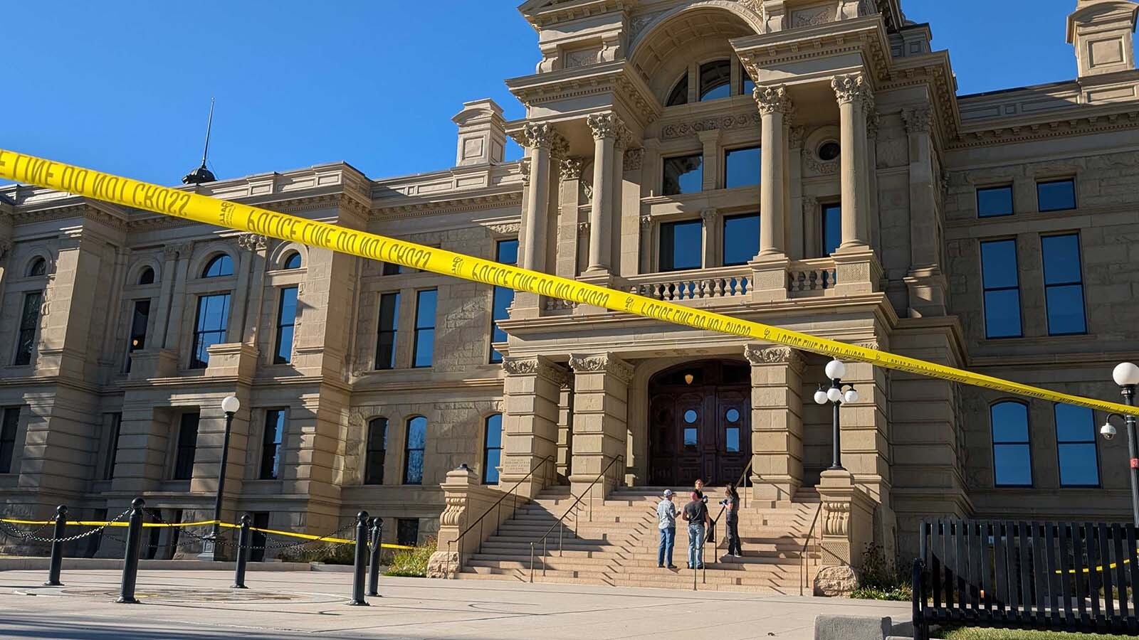 Behind yellow crime scene tape, a group of people in plain clothes investigate on the steps of the Wyoming Capitol on Tuesday during an evacuation and lockdown of the building sparked by the report of an improvised explosive device in the building.