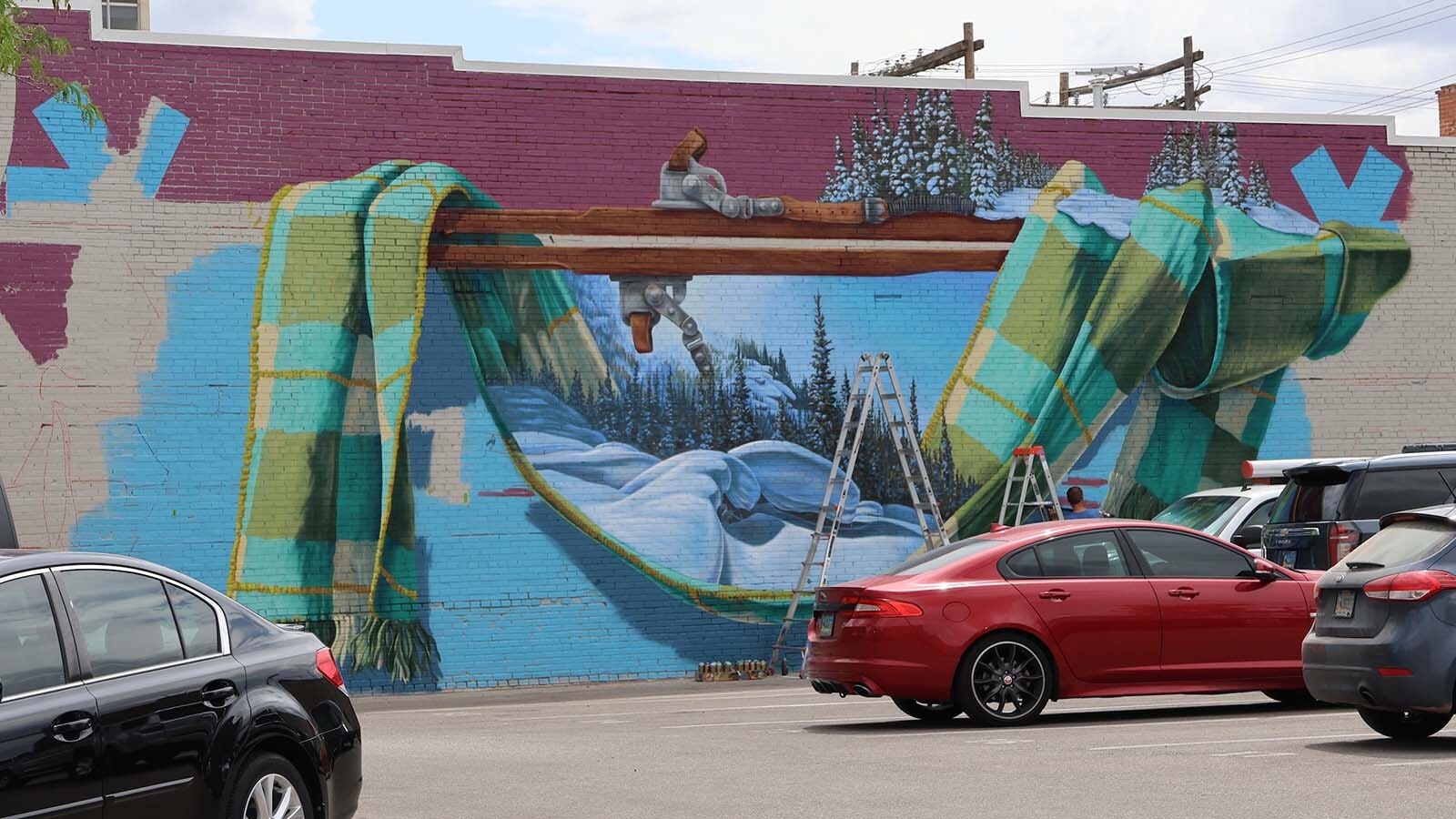 The mural honoring volunteers who made skiing on Casper Mountain what it is today includes a ski scene above the scarf as artist Dan Toro makes progress through the week.