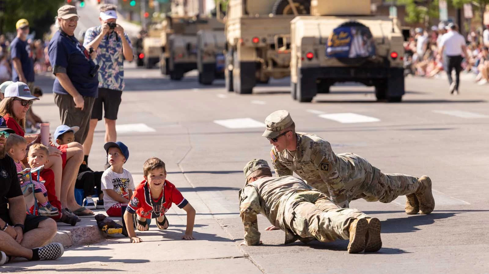 Military members do push-ups with kids along the route of Cheyenne's 250th Fourth of July Parade.