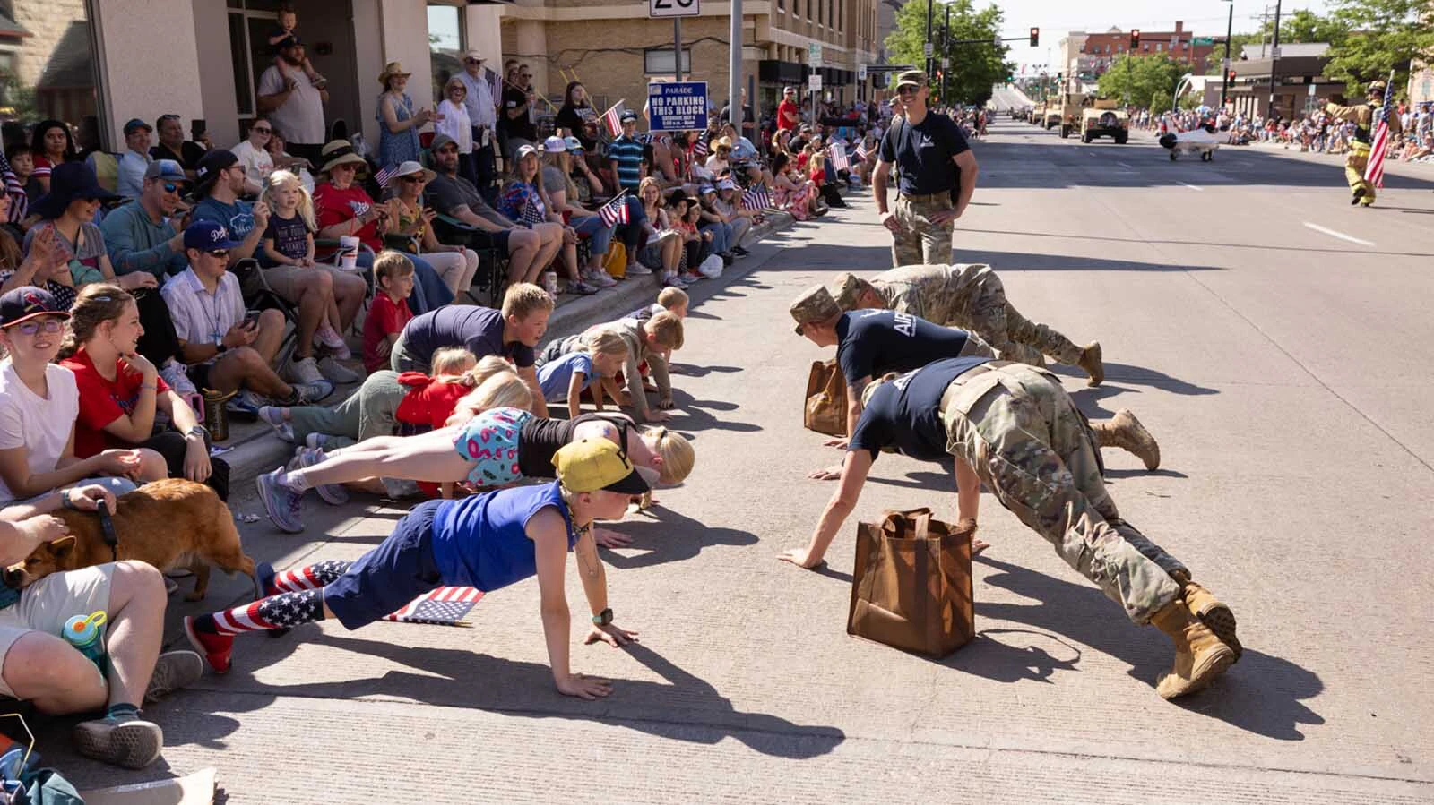 Military members do push-ups with kids along the route of Cheyenne's 250th Fourth of July Parade.