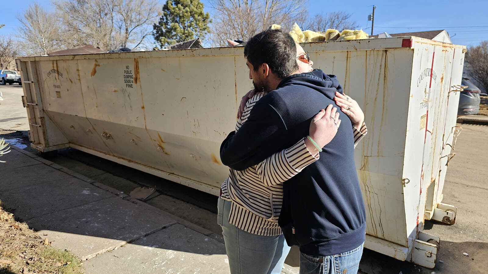 Landyn Medina gives Phylicia Peterson a hug Tuesday morning in front of a dumpster that's quickly filling up with waterlogged insulation and drywall, as well as her now nonfunctional washing machine. Peterson's home has sustained $80,000 in damages after a city water main busted and inundated several homes in the area of Cahill Park.