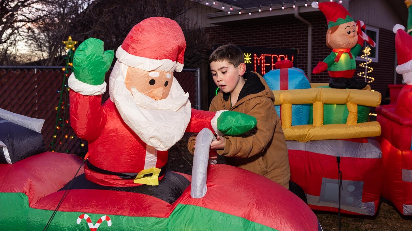 Carsen Bartow puts inflatable Christmas decorations in place. The display is all about Santa and fire trucks.