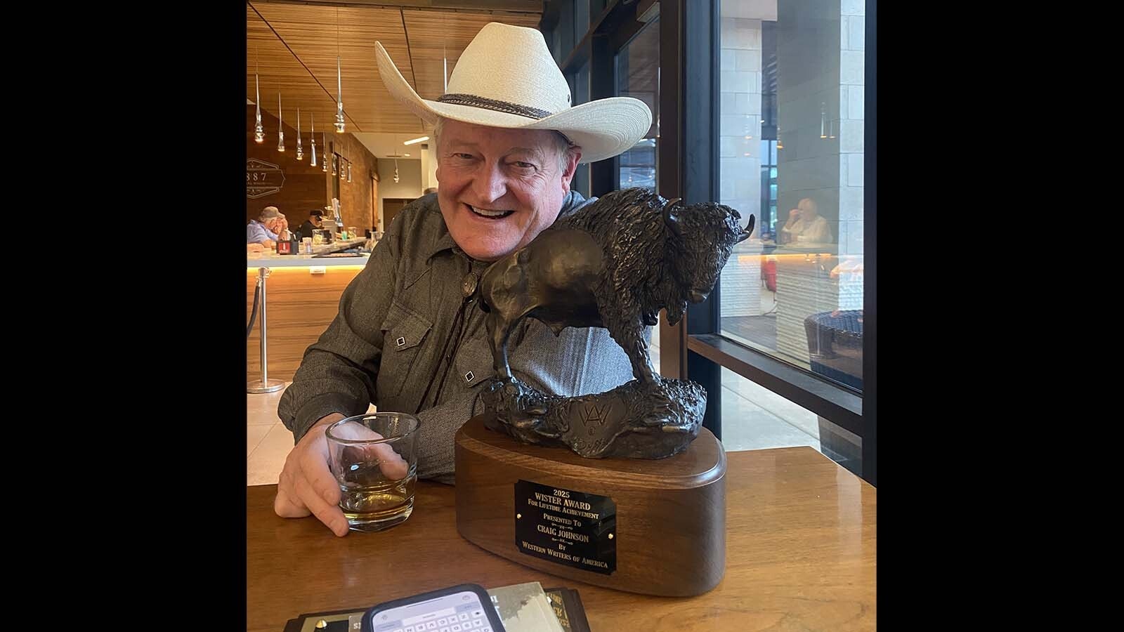 xWyoming author Craig Johnson creates his popular “Longmire” mystery series in a tiny UCross cabin loft he built himself. In 2025, he was recognized with four lifetime achievement awards from prestigious writing and Western organizations. Here he toasts the Owen Wister Award he was given in 2025 by the Western Writers of America.