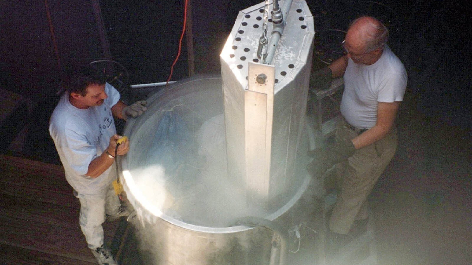 A pair of technicians lower a body into a cryonics vessel.
