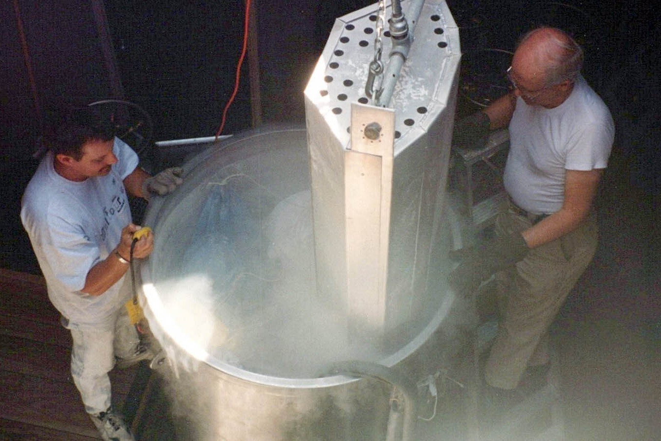 A pair of technicians lower a body into a cryonics vessel.