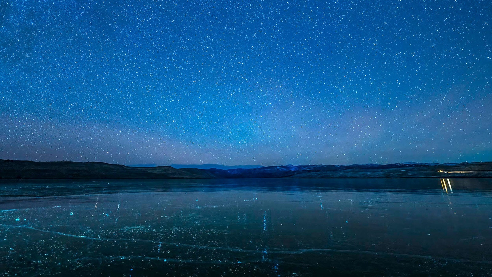 The edge of a perfectly clear sheet of ice on Fremont Lake is just visible under the stars of a cold Wyoming night.