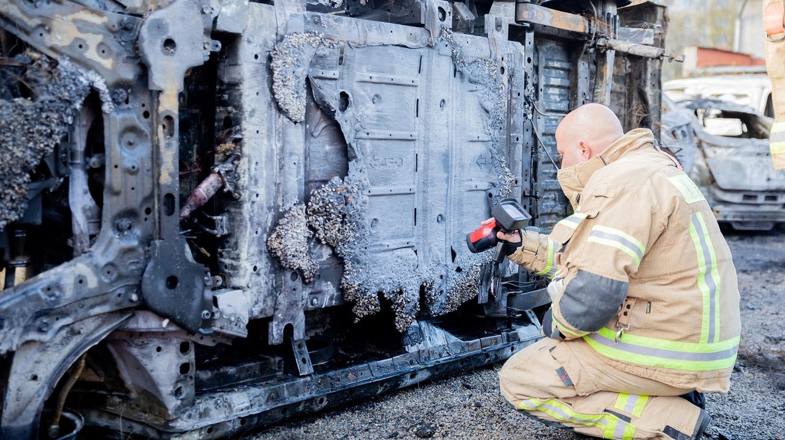 A firefighter inspects the underside of an electric vehicle after it burned.