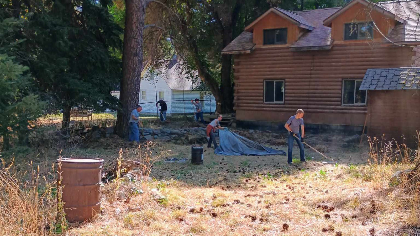 Volunteers work to rake up pine needles and pine cones, reducing fuel around this home in Story.