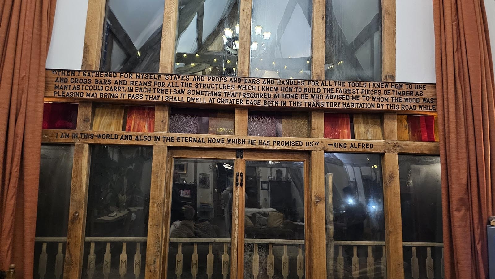 A quote from King Alfred decorates the picturesque windowed wall of Cyning Meadowcroft's medieval-style, cruck-constructed home in Happy Valley. The windows look out on mountains in the distance.