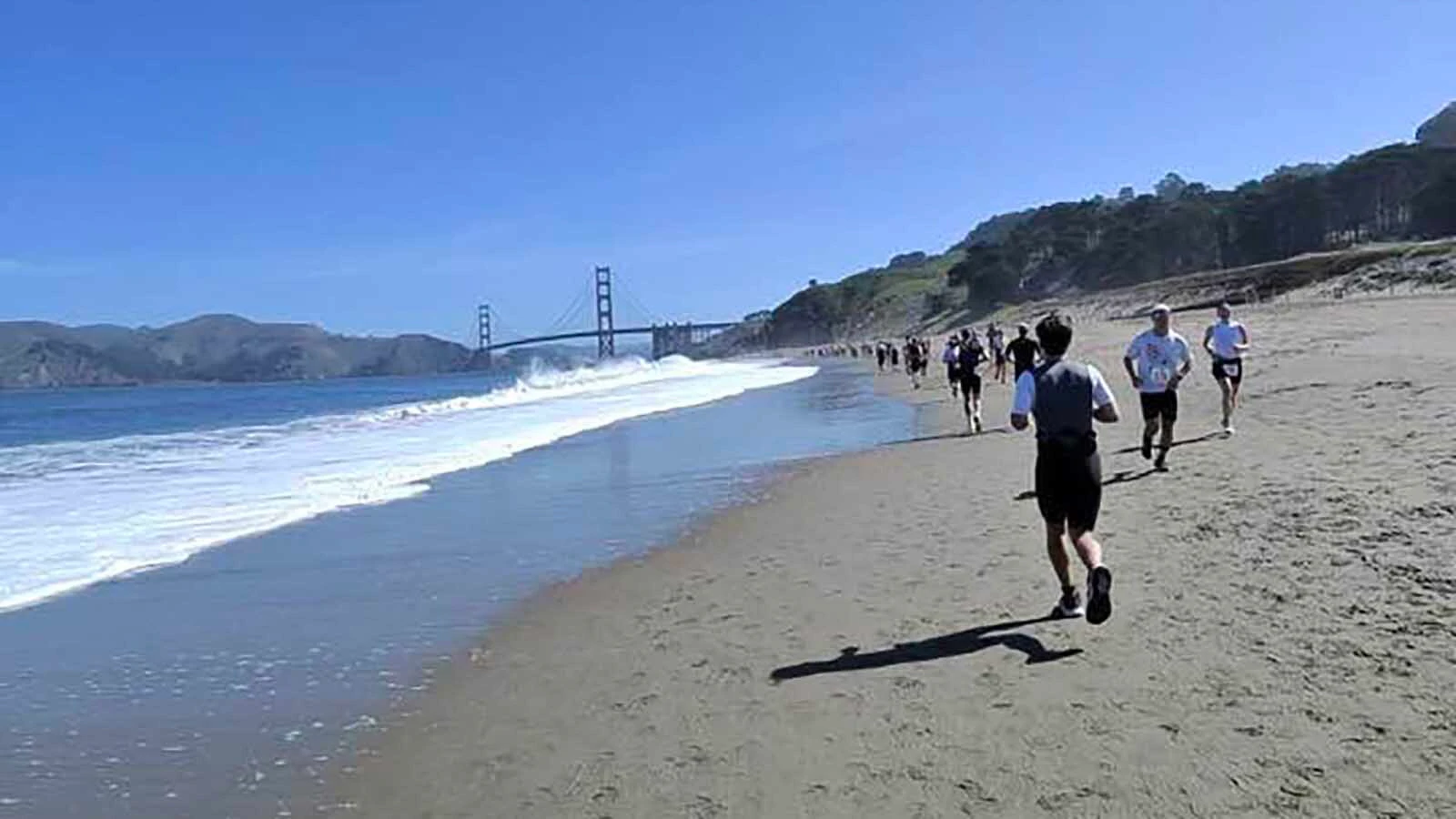 Participants race along the beach toward the Golden Gate Bridge.