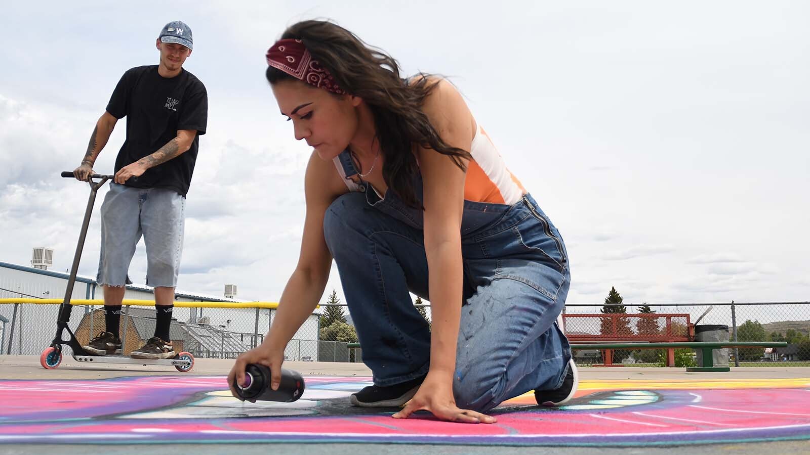 Evanston artist Michelle ‘Chely’ Gomez adds a few touchups to her work at the Evanston Skate Park, as local scooter enthusiast Cutter Nicholson looks on.