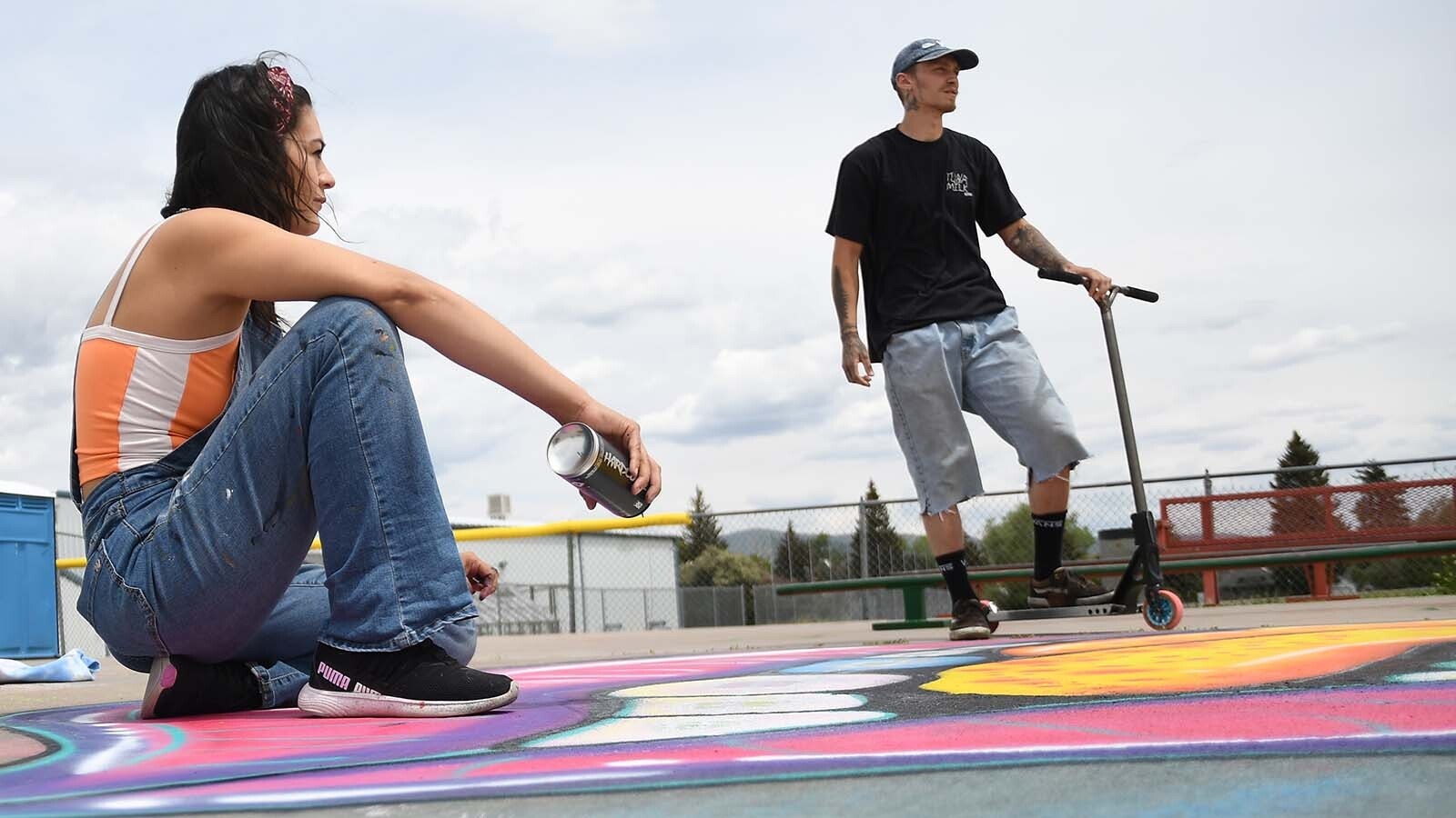 Evanston artist Michelle ‘Chely’ Gomez adds a few touchups to her work at the Evanston Skate Park, as local scooter enthusiast Cutter Nicholson looks on.