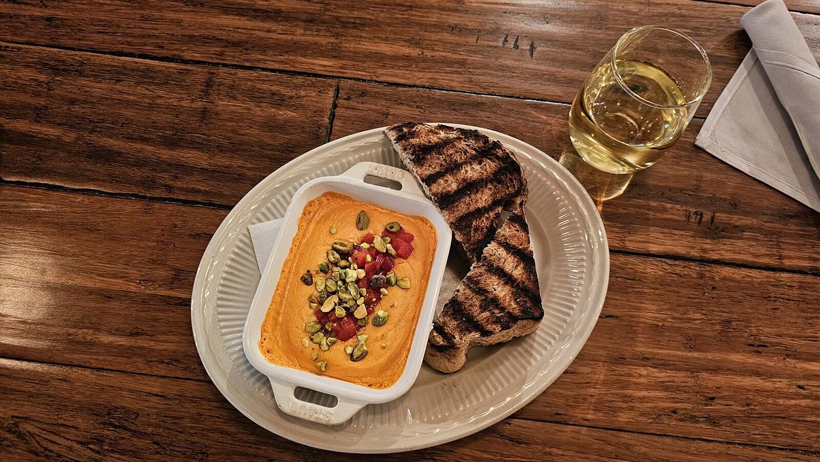 A cheesy dip garnished with nuts and tomatoes, served with grilled sourdough bread.