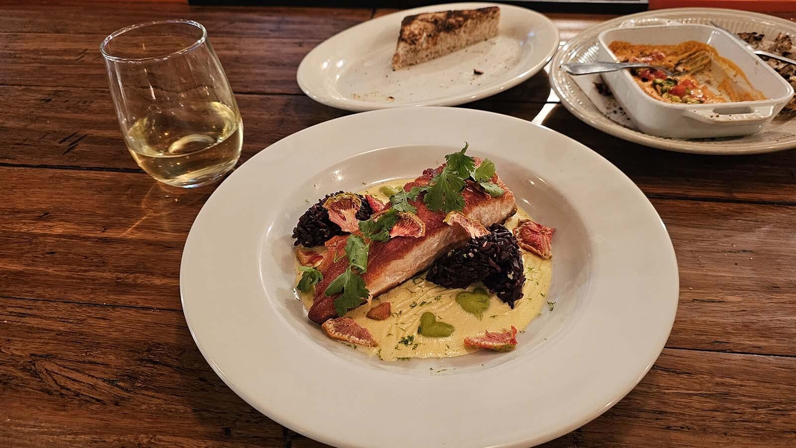 Pan-seared Atlantic salmon floats on a swirl of lemongrass and chili hollaindaise. Two dollops of black onigiri, garnished with tomato chips and herbs. Little heart-shaped puree of lime and pea finish out the dish, along with some shavings of bottarga, a Sicilian delicacy made by curing and drying fish roe.
