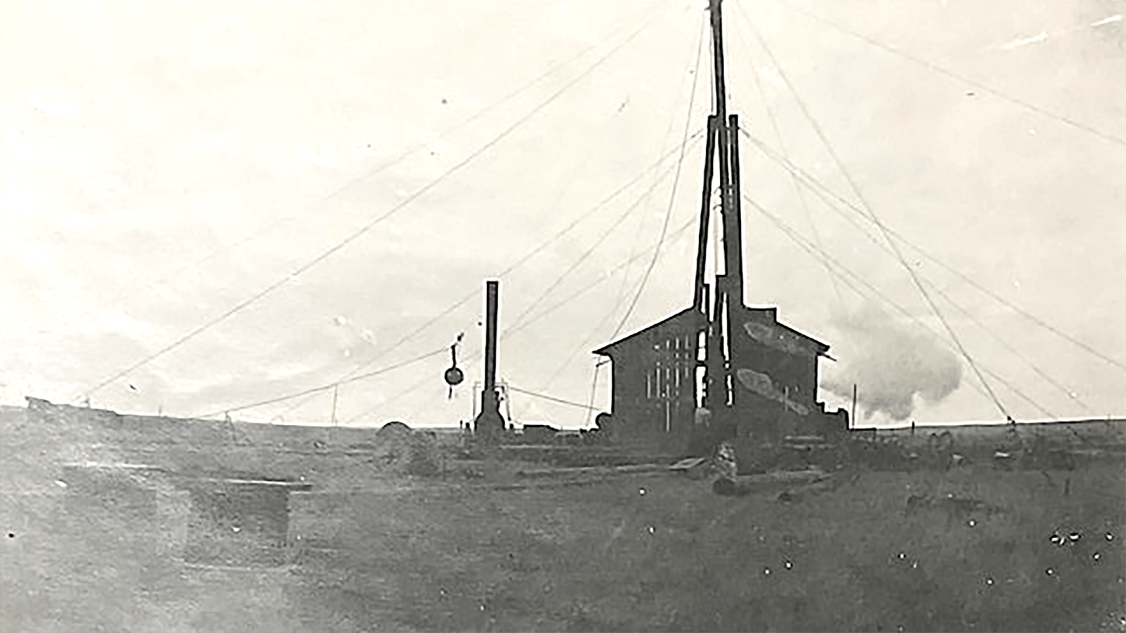 An oil well drilling rig and unidentified building in Wyoming’s early oil patch.