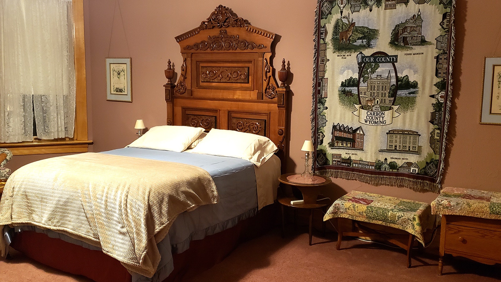 The Rose Room features a large bed with a wall hanging celebrating Carbon County. The Ferris Mansion is one of the buildings portrayed on the wall hanging.