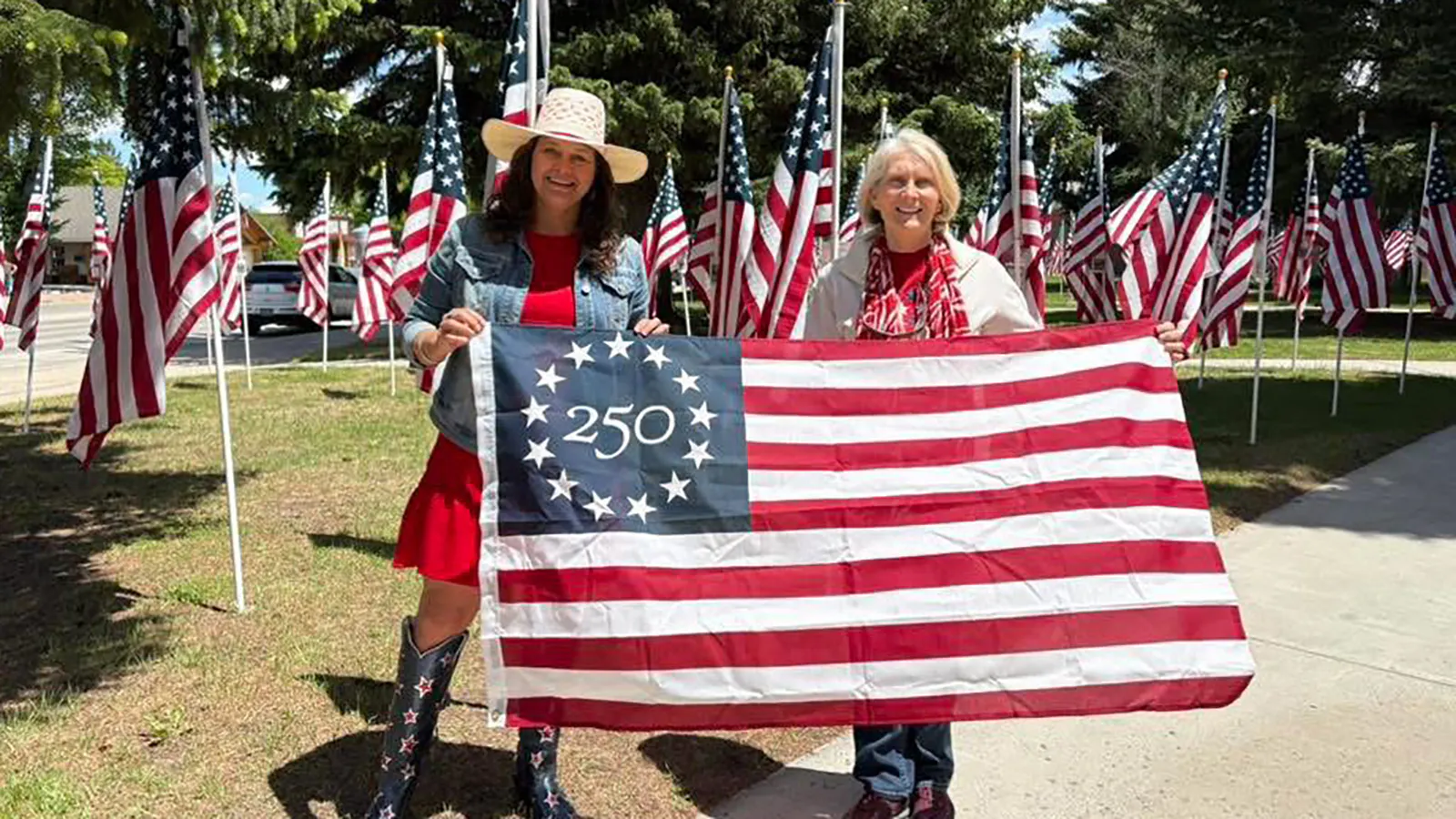 Cody Chamber of Commerce Director Jennifer Thoma (left) and Sandy Newsome, chair of the  Wyoming Semiquincentennial Planning Task Force, hold the Betsy Ross flags that will be displayed on Sheridan Avenue through the summer.