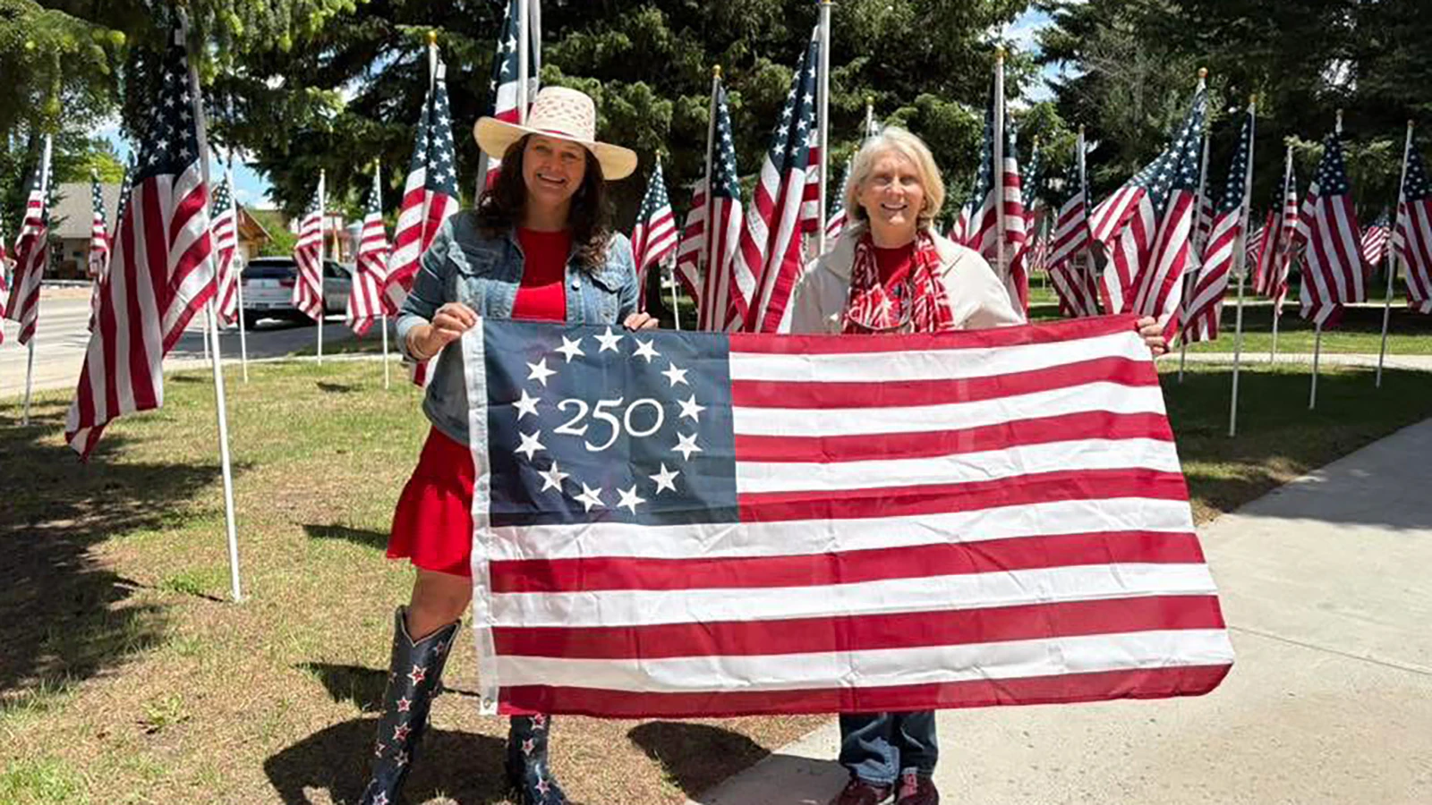 Cody Chamber of Commerce Director Jennifer Thoma (left) and Sandy Newsome, chair of the  Wyoming Semiquincentennial Planning Task Force, hold the Betsy Ross flags that will be displayed on Sheridan Avenue through the summer.
