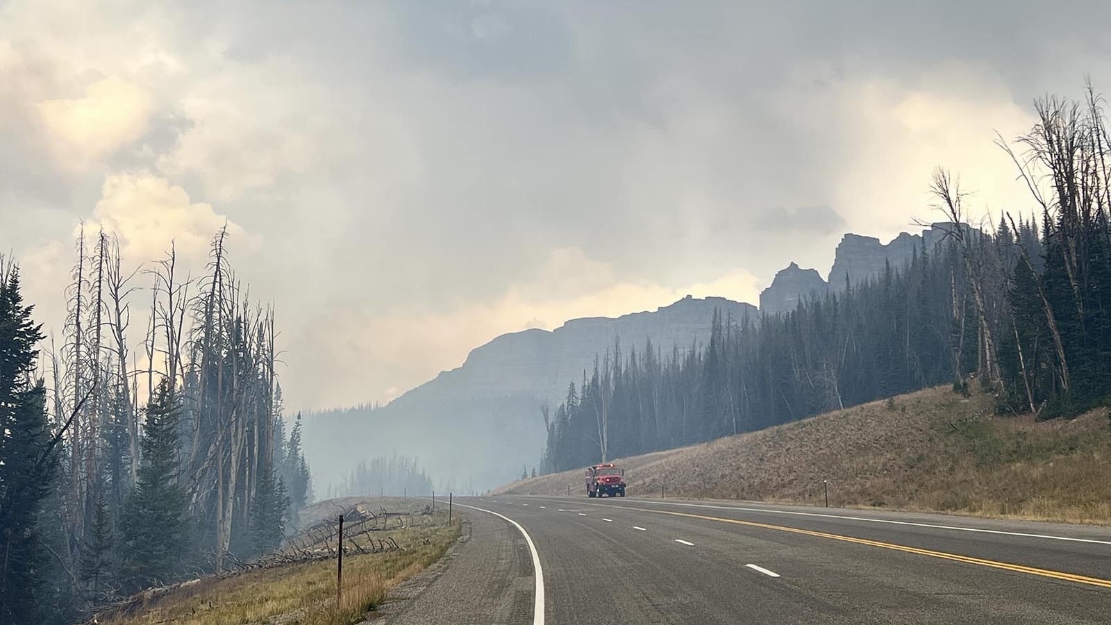 A fire truck drives on a closed Highway 26/287 over Togwotee Pass with smoke from the Fish Creek Fire.