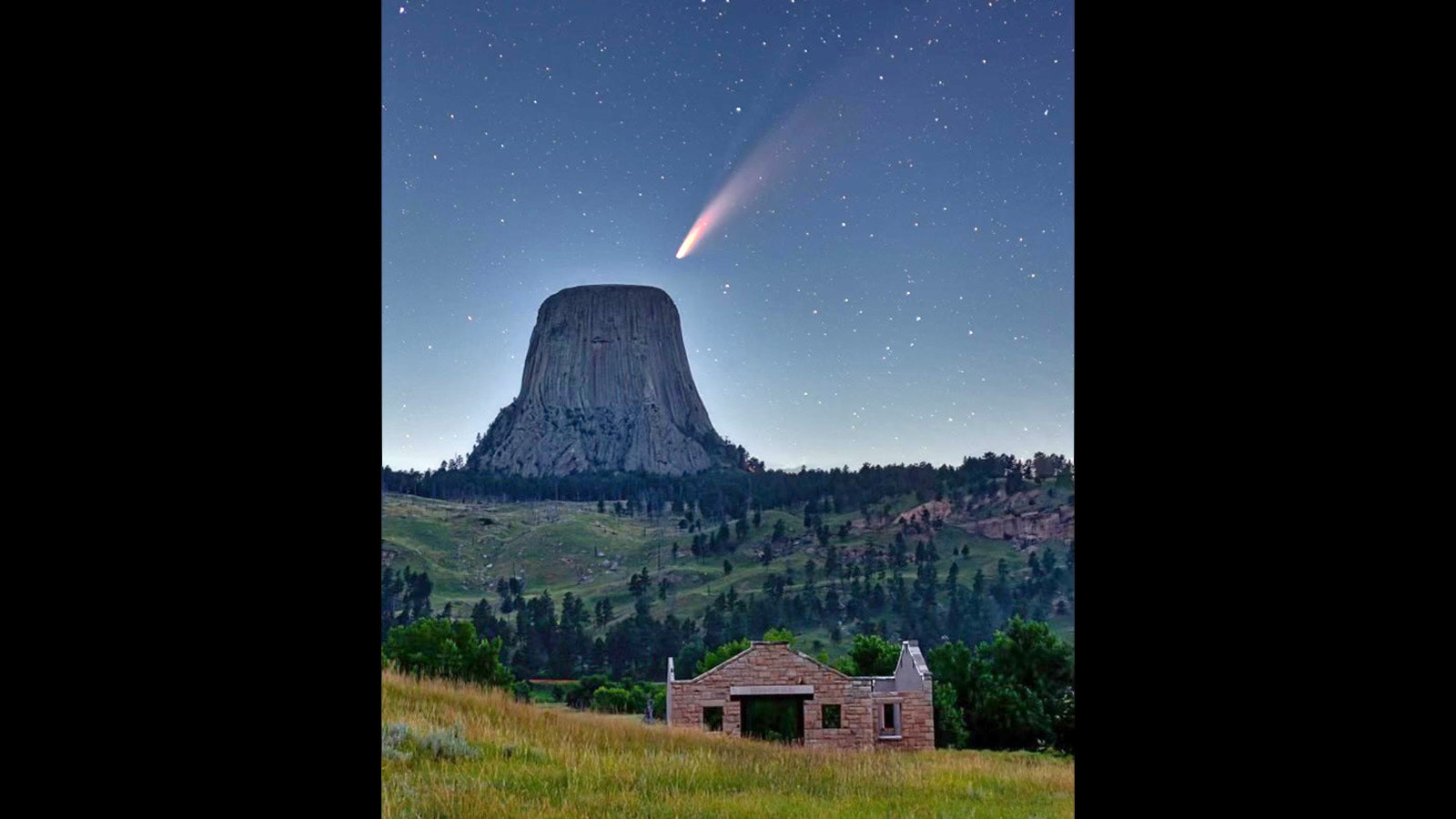 A shooting star over Devils Tower with the historic Toomeys Mill building in the foreground.