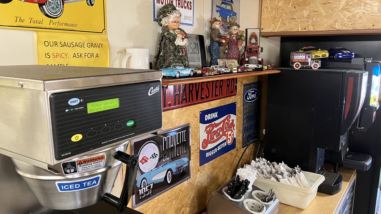 Classic car, truck, and soft drink signs fill the wall between the soft drink and coffee machines at the diner.