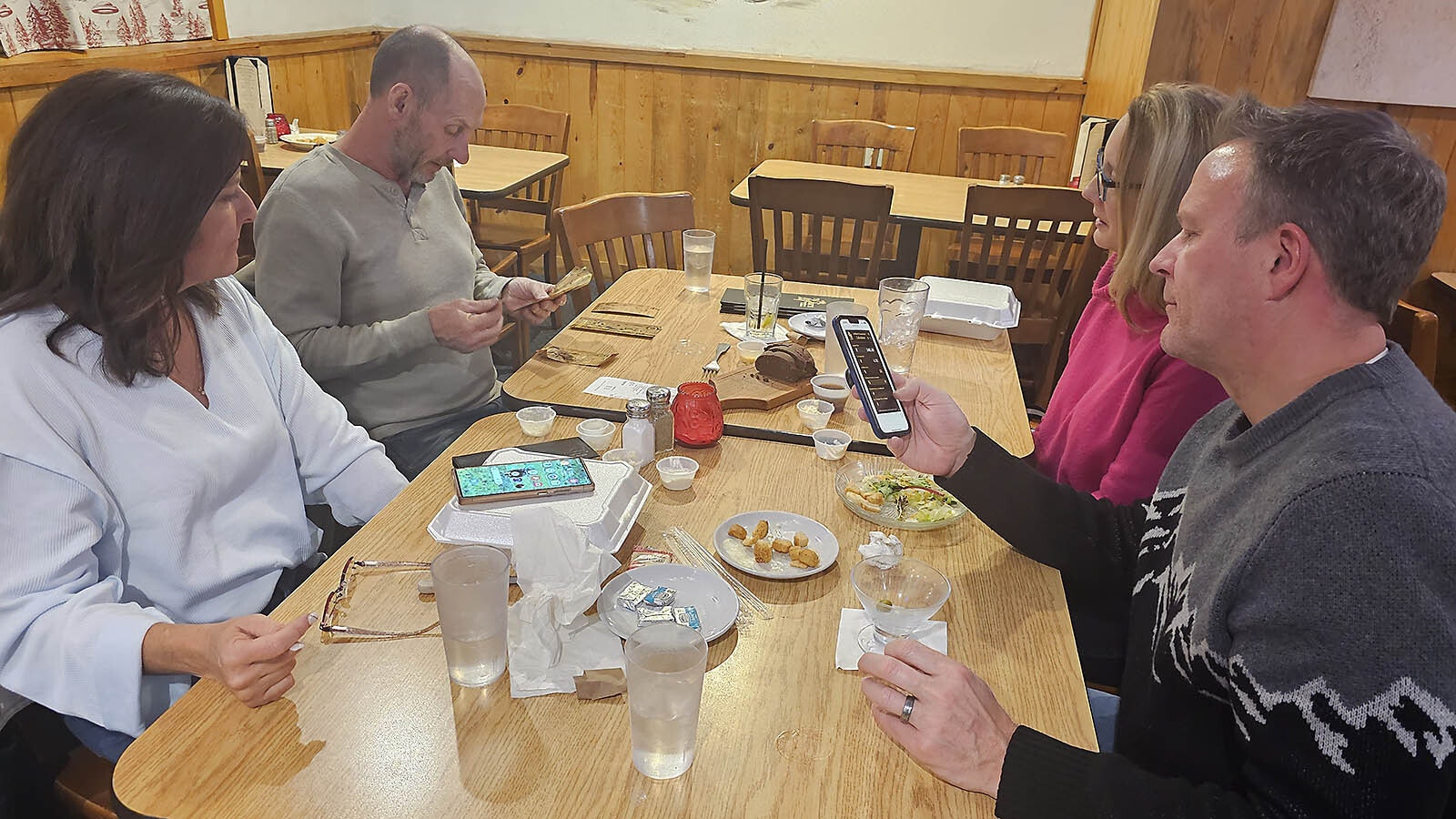 Laura Hoch, from left, watches as her husband Chris sorts through their goldbacks while across the table, Caroline Walter watches and her husband, Dan Walter, checks exchange rates using the Goldback Company's app.