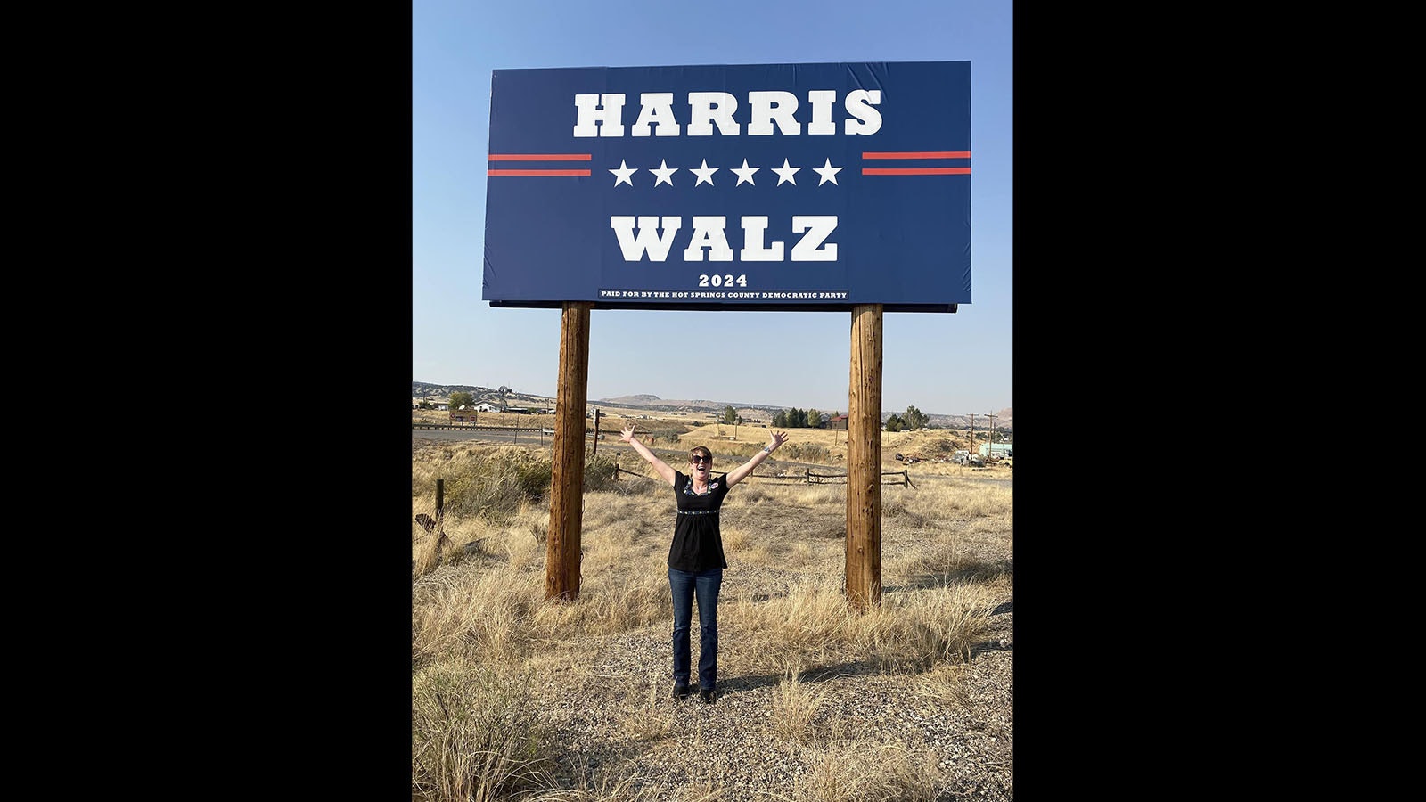 Hot Springs County Democratic Party Chair Kim Bartlett stands next to the billboard for Vice President Kamala Harris she organized.